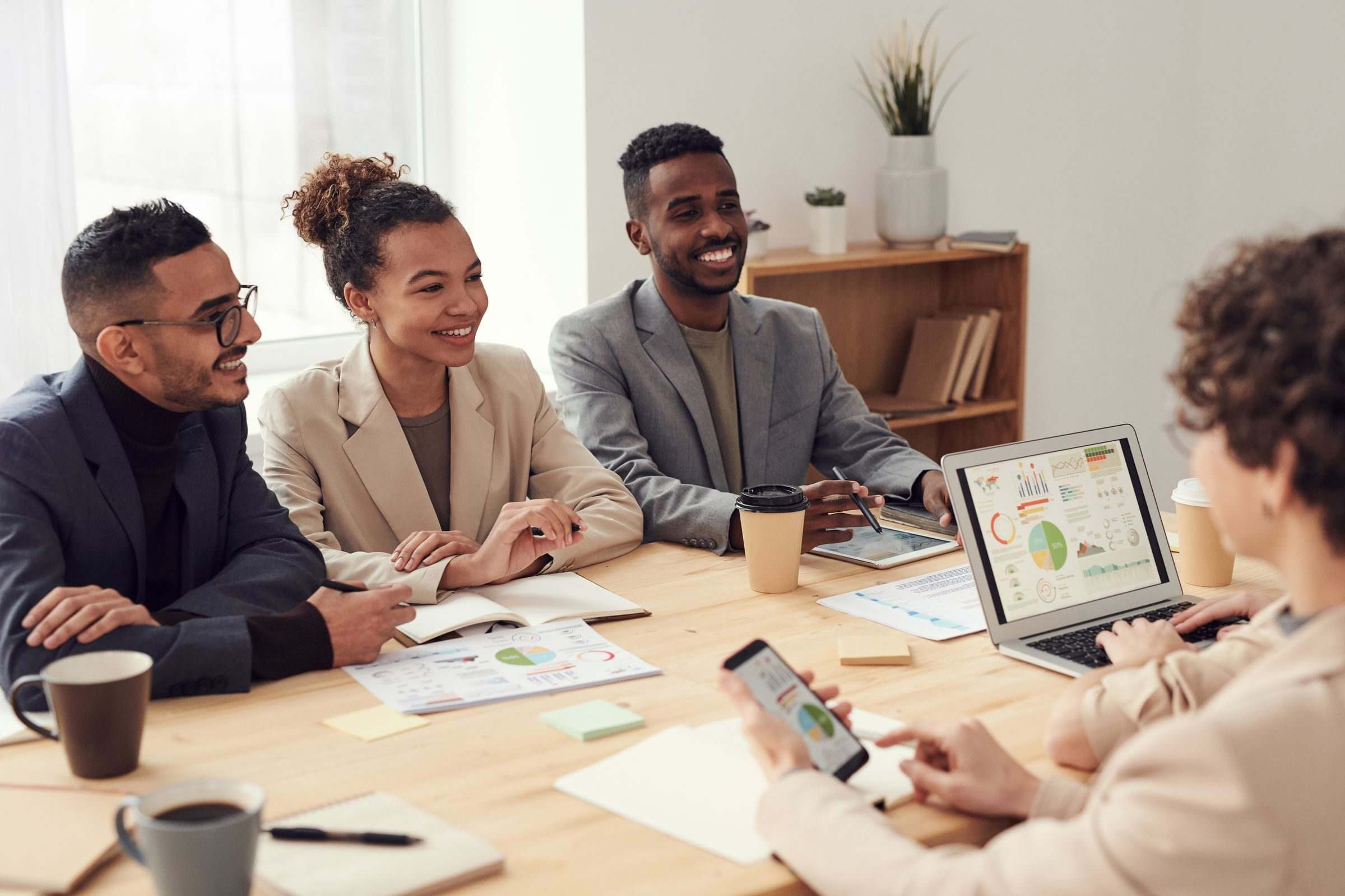Colleagues smiling around a table as they review charts on a laptop, tablet and phone
